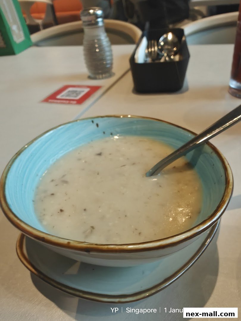 A bowl of creamy mushroom soup with a spoon in a restaurant setting.