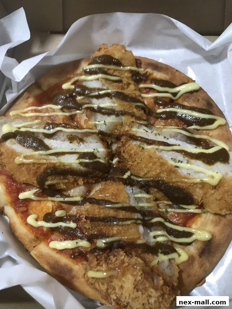 A close-up view of a unique curry pizza topped with fried chicken and sauces.