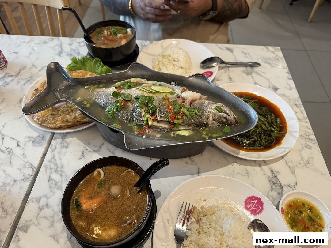 A table laden with Thai dishes, including a whole steamed fish, tom yum soup, and stir-fried vegetables.