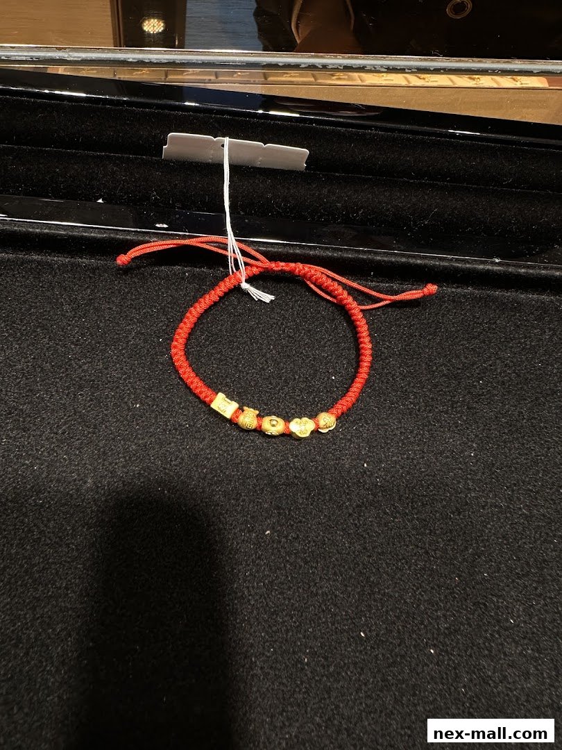 A red string bracelet with gold charms displayed on a black surface.