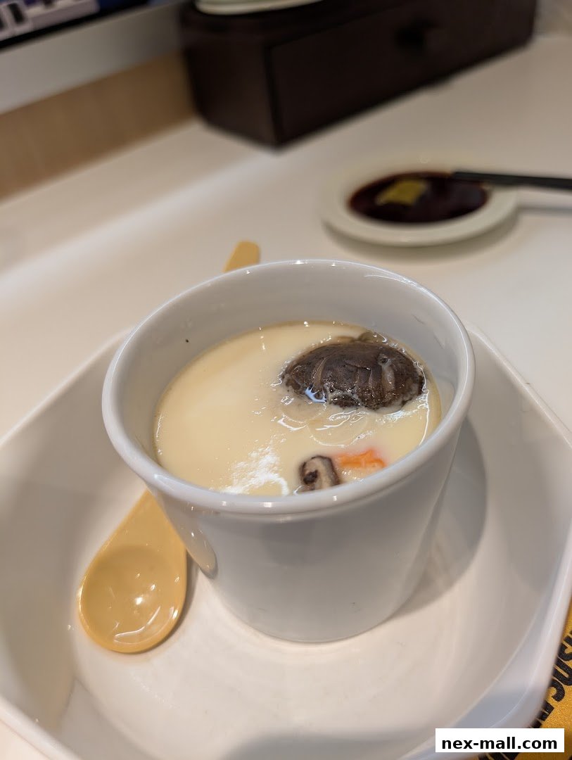 A close-up of a steaming cup of chawanmushi with a mushroom and carrot garnish.