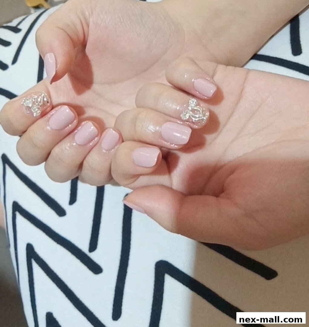 Close-up of hands with elegant light pink nails adorned with sparkling embellishments.