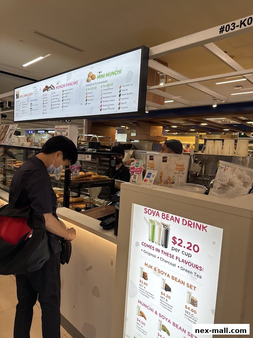 A customer orders at a Munchi Pancakes counter with a menu board and drink promotions.