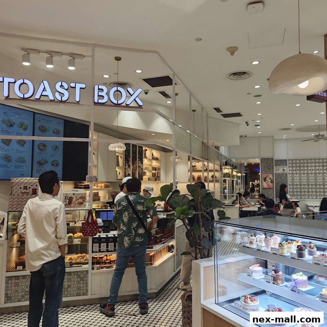 Interior view of Toast Box NEX with customers ordering and display of pastries and cakes.