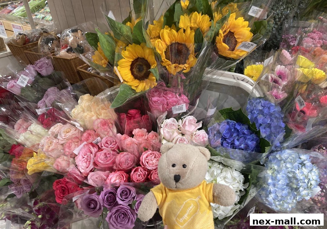 A colorful display of fresh flowers including roses, sunflowers, and hydrangeas, with a teddy bear.