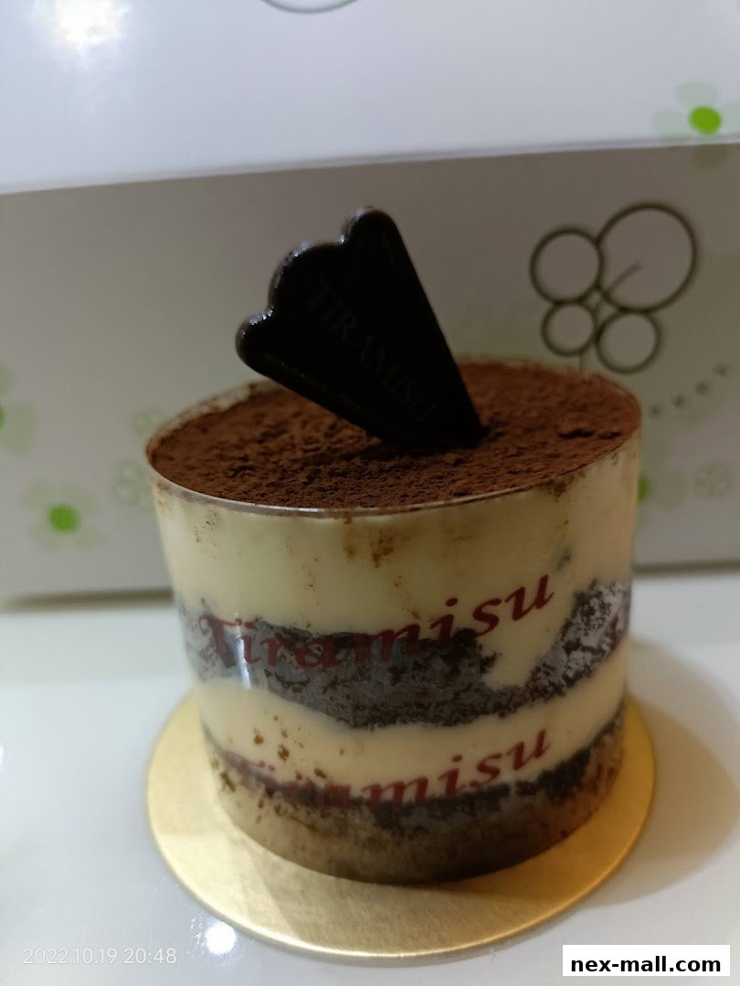 A delicious tiramisu dessert in a clear cup with cocoa powder and a chocolate garnish.