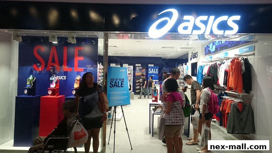 The entrance of an ASICS store with a large 'SALE' banner and displays of athletic shoes and apparel.