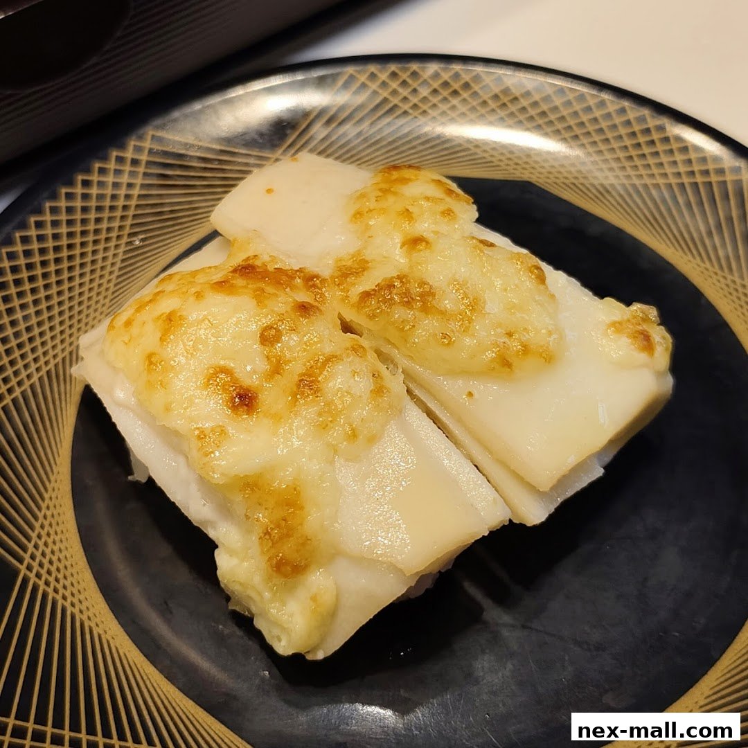 Close-up of two pieces of sushi topped with melted cheese on a black plate.