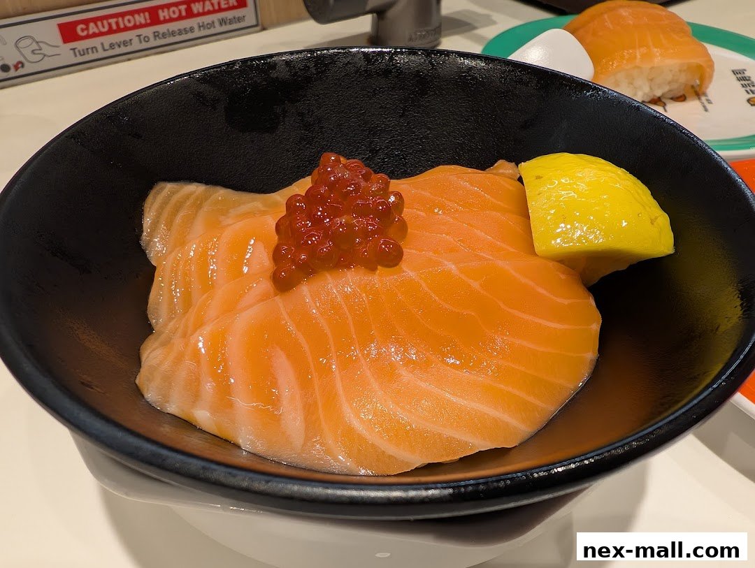 A close-up of a salmon donburi bowl with ikura and a lemon wedge.
