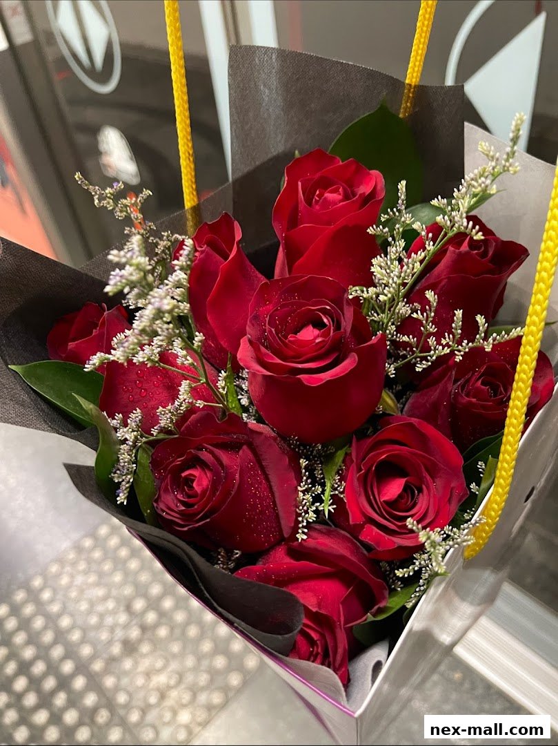 A bouquet of deep red roses with delicate white filler flowers, presented in a stylish gift bag.