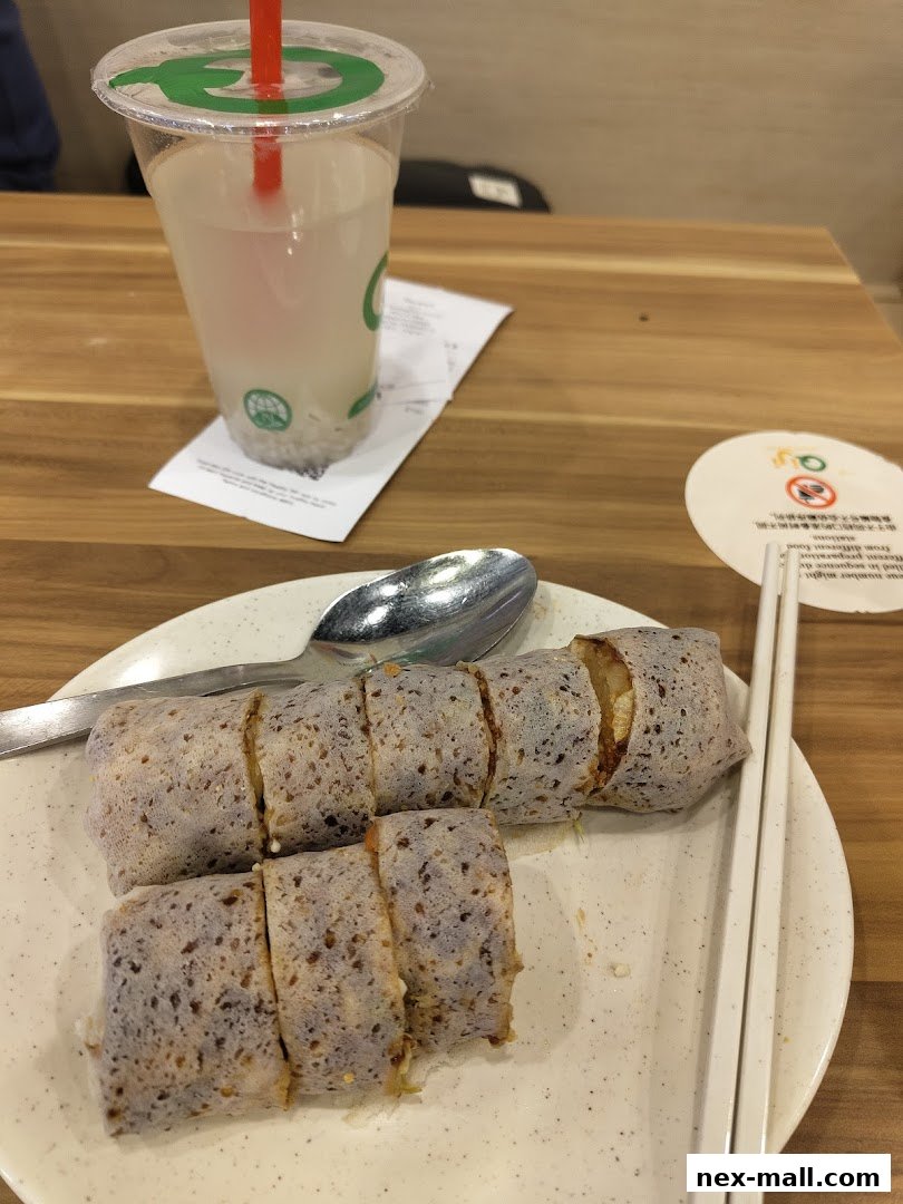 A plate of sliced spring rolls with a drink and utensils on a wooden table.