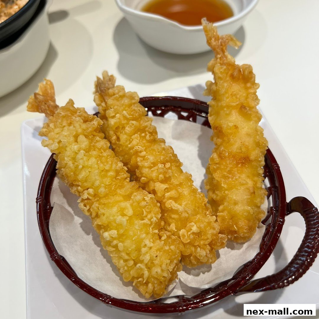 Three crispy fried shrimp tempura served in a basket with a dipping sauce in the background.