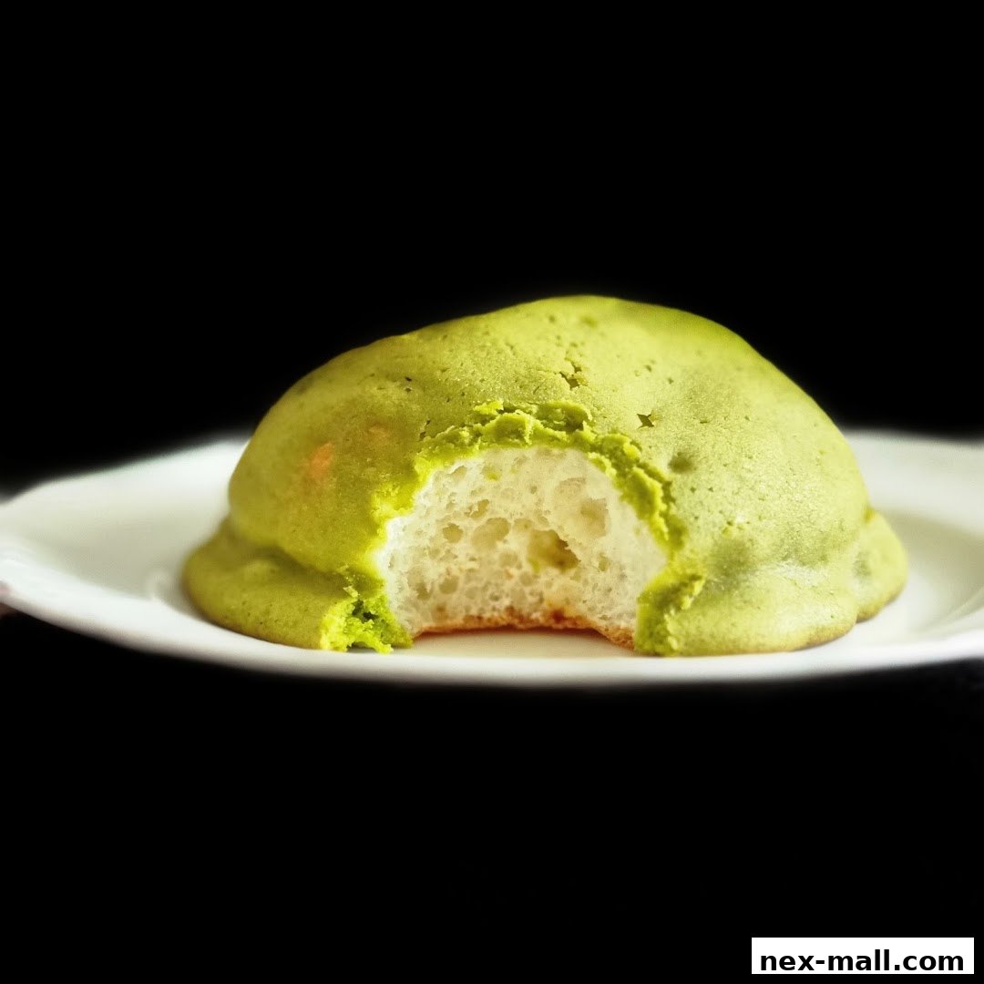 A close-up of a green melon pan with a bite taken out, on a white plate.