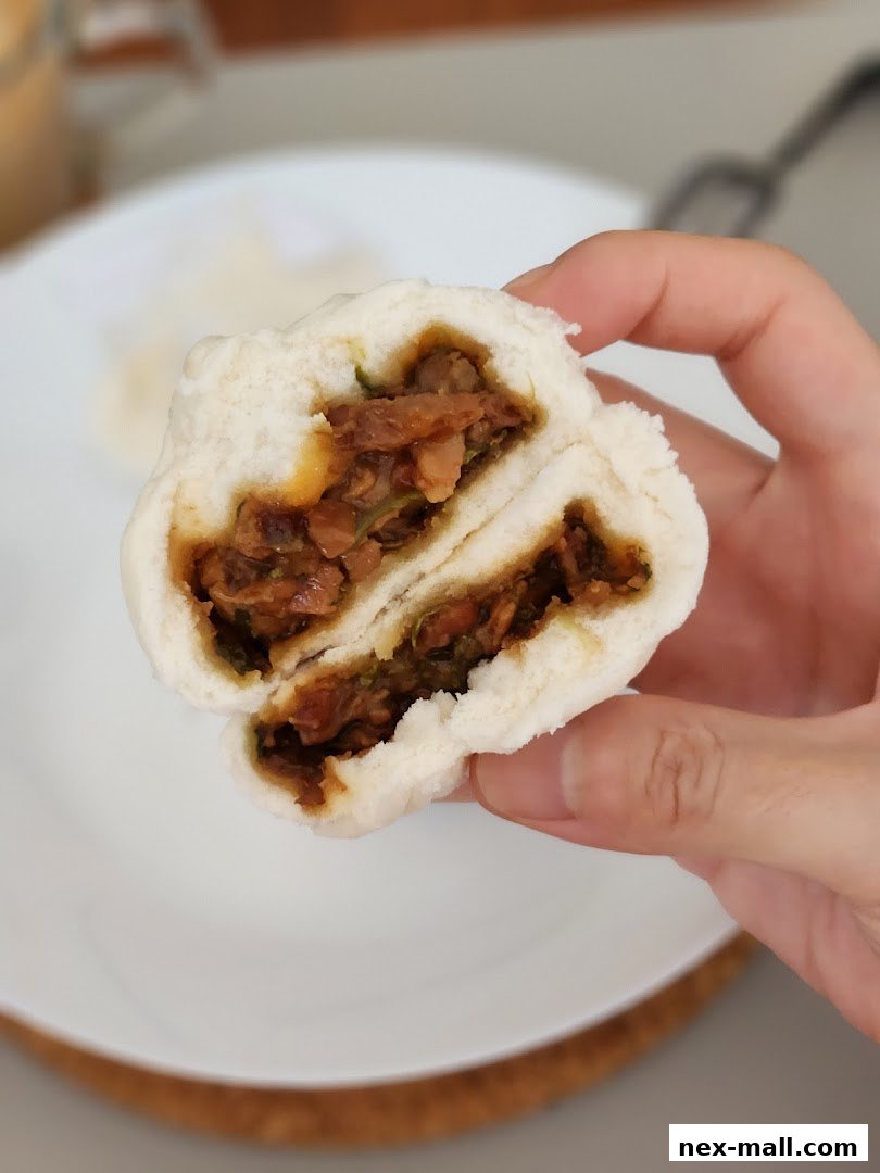 A hand holds a halved steamed bun filled with savory meat and vegetables.