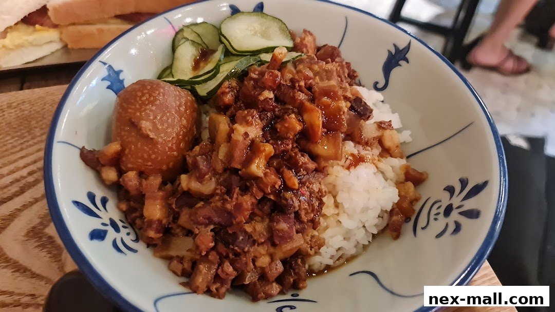 A close-up of a bowl of braised pork rice with a braised egg and cucumber slices.