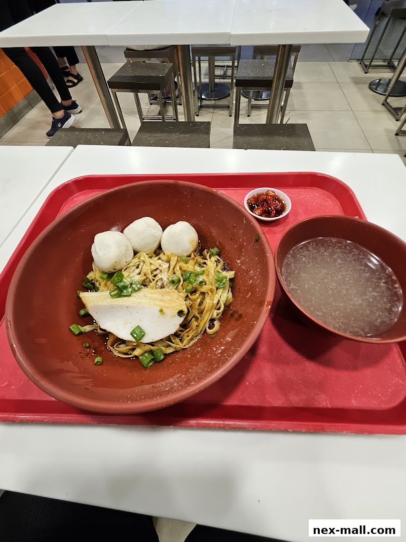 A bowl of noodles with fish balls and a slice of fish cake, served with soup and chili.