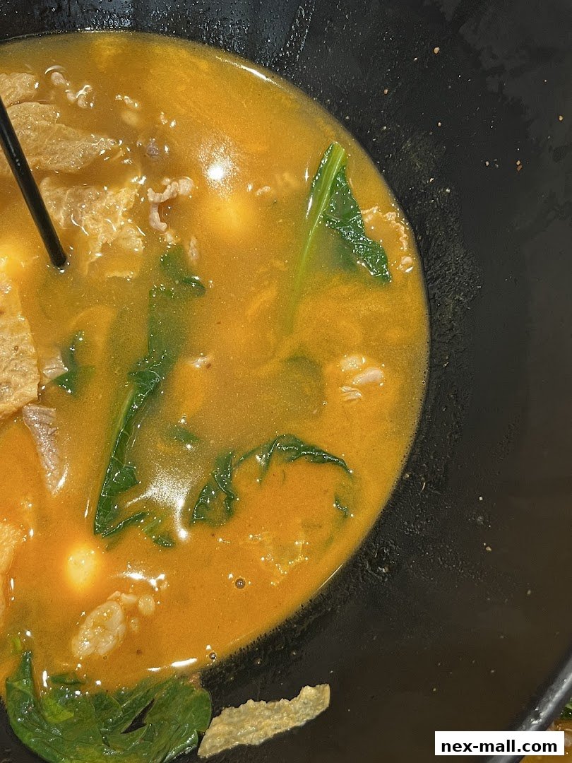 A close-up of a steaming bowl of Mala Tang with meat, vegetables, and tofu skin.