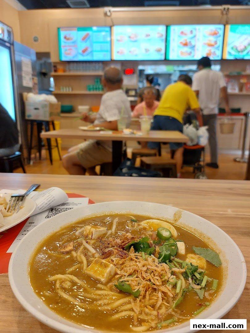 A close-up of a bowl of noodles with people dining in the background.