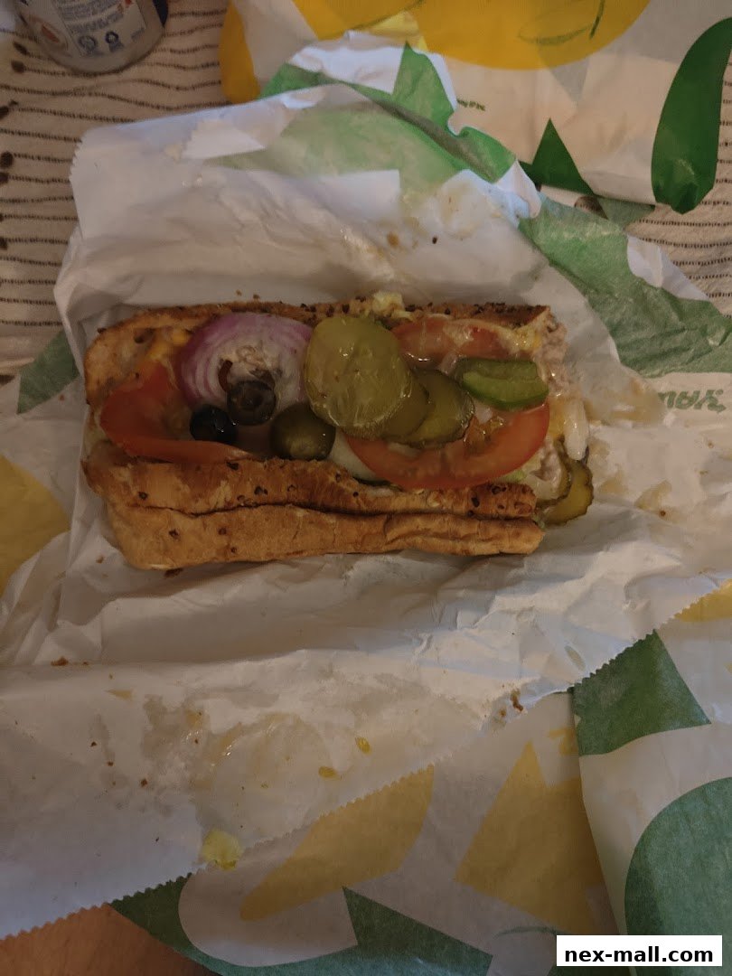 A Subway sandwich with various toppings on a paper wrapper.