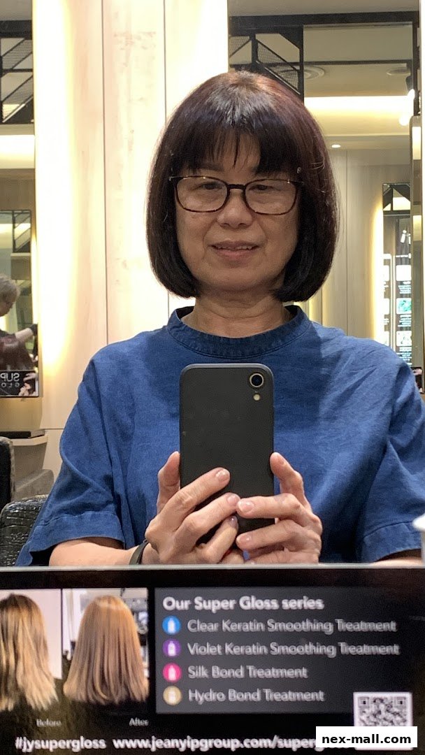 A woman with glasses takes a selfie in a salon, showcasing hair treatments.