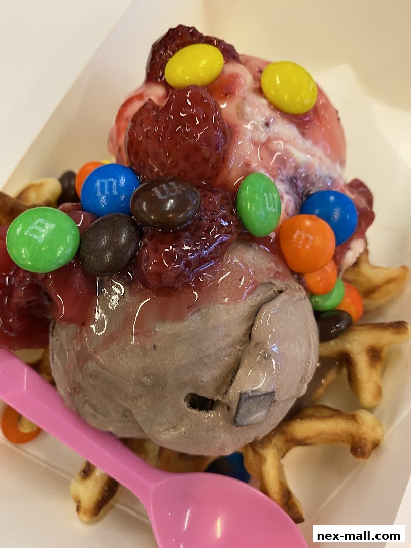 A close-up of a delicious ice cream sundae with waffle pieces, strawberries, and M&Ms.