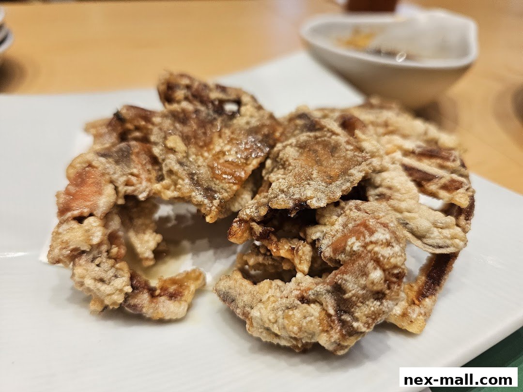 Crispy fried soft shell crab served on a white plate with a dipping sauce in the background.