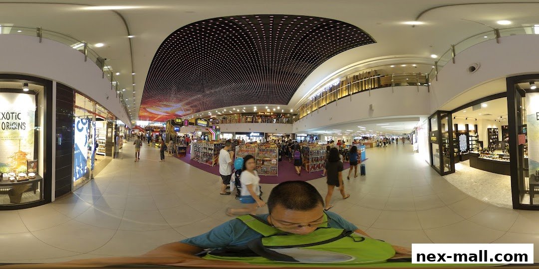 A wide-angle view of a shopping mall interior with various shops and shoppers.