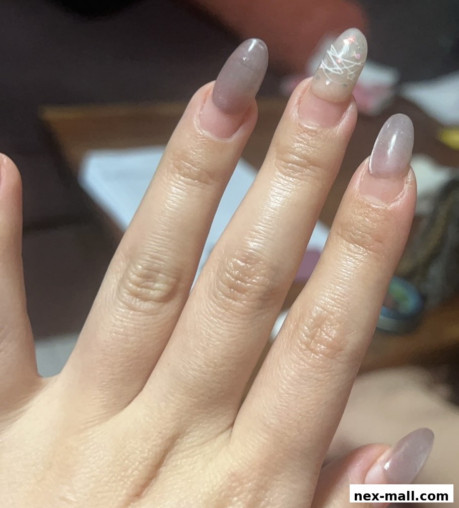 Close-up of a hand with oval-shaped nails, some with a sheer polish and one with intricate white line art.