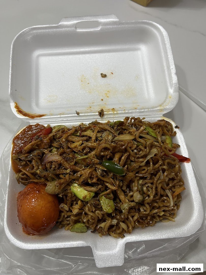 A take-out container filled with noodles, anchovies, vegetables, and a fried egg.