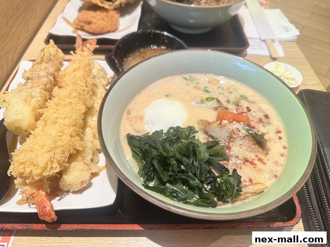 A close-up of a creamy udon soup with tempura shrimp and other toppings.