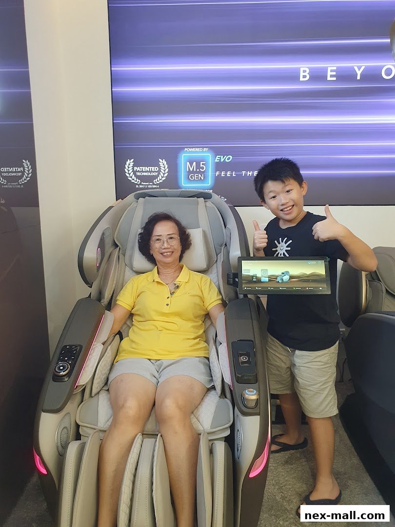 A woman sits in a massage chair while a boy gives a thumbs up.