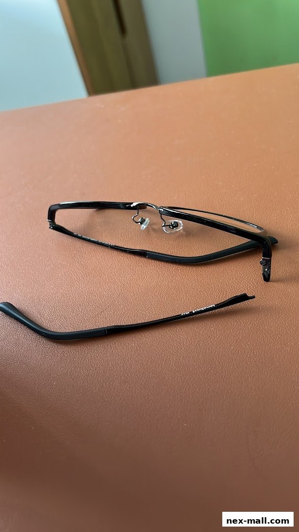 A pair of broken black eyeglasses lying on a brown surface.