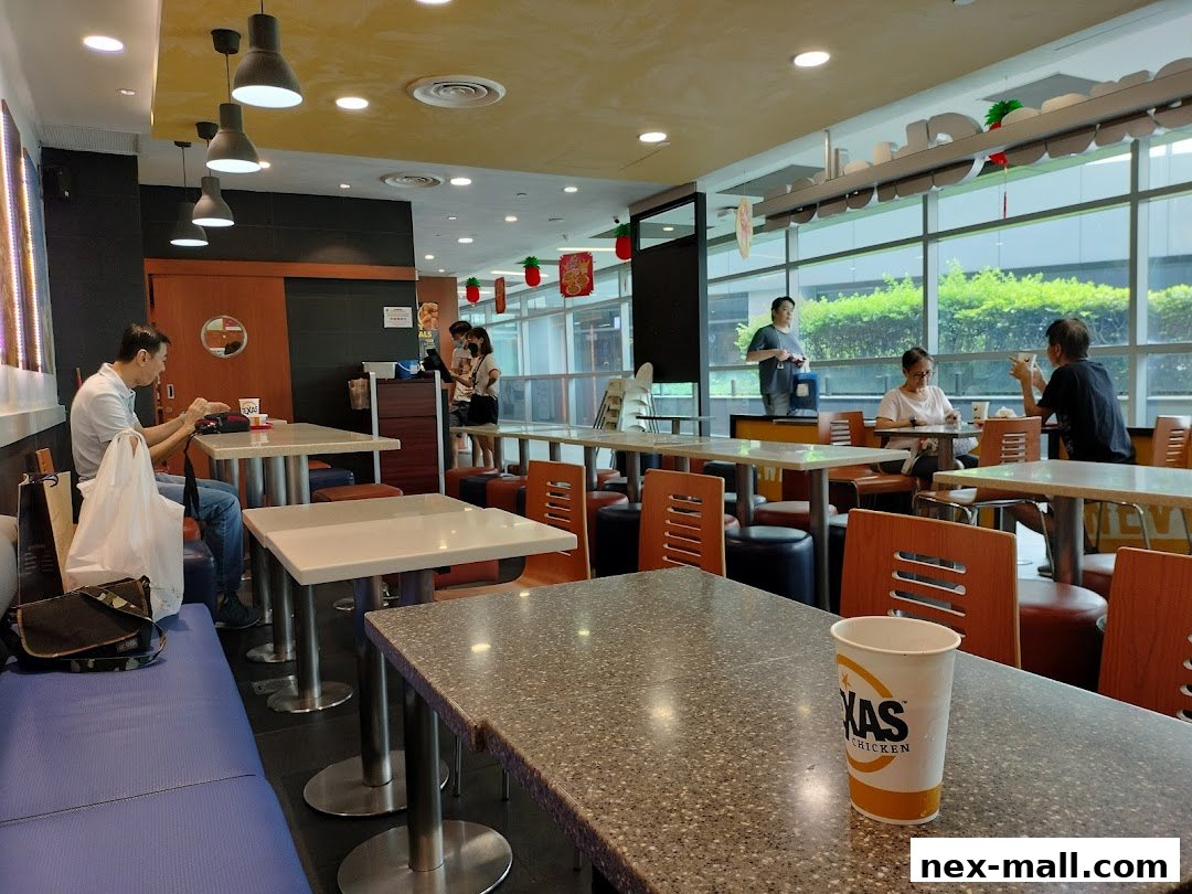 Interior of Texas Chicken NEX with customers dining at tables and a branded cup in the foreground.