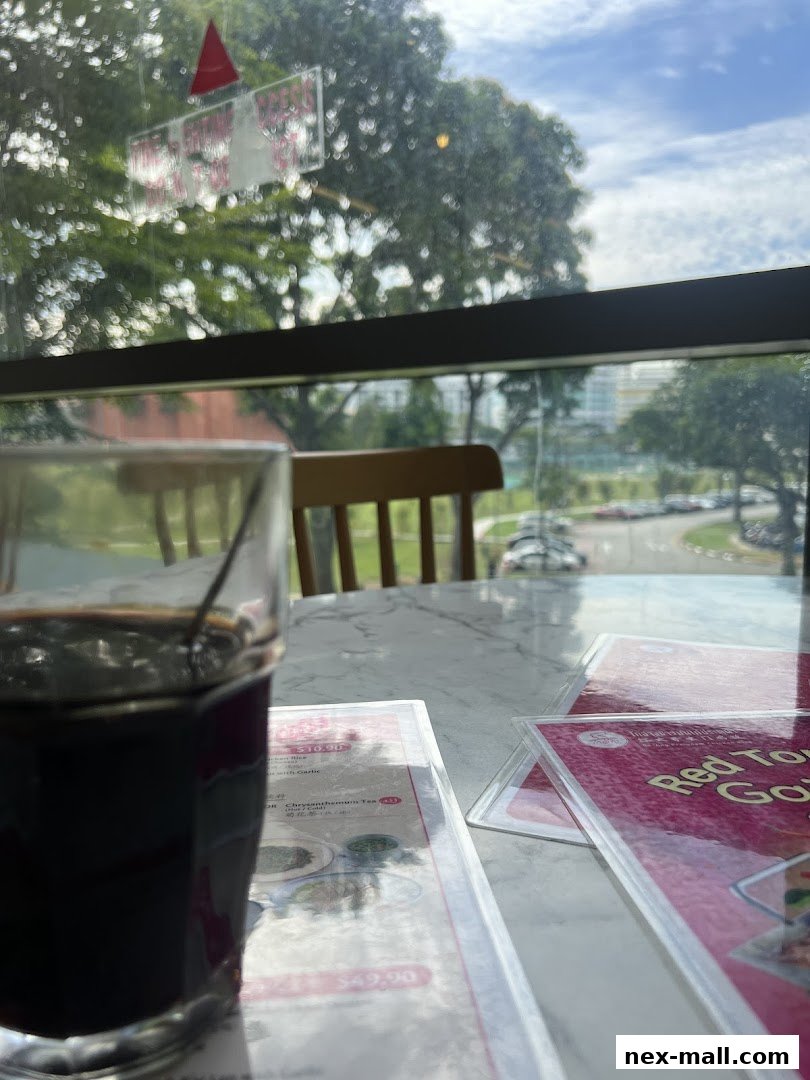 A table with a drink and menus, viewed through a window with trees and sky.