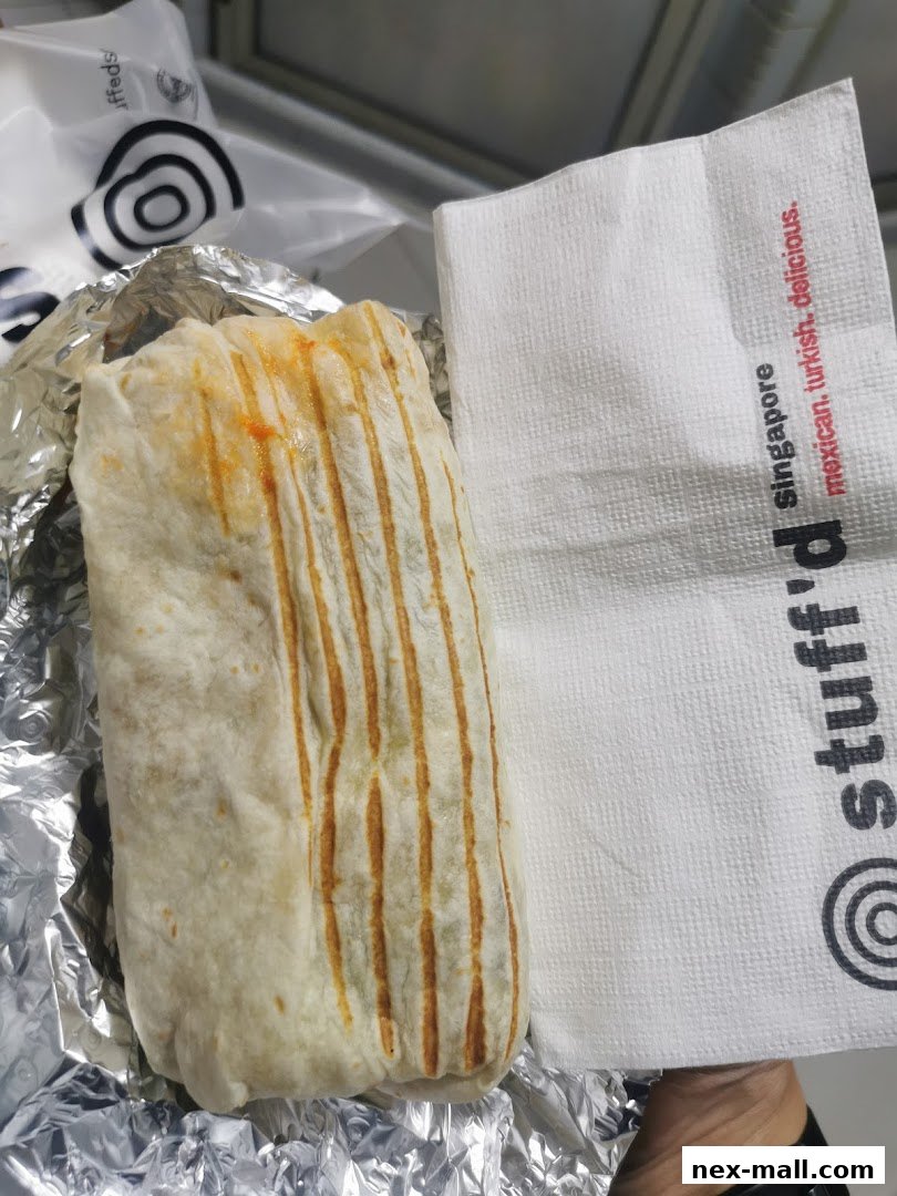 A close-up of a grilled wrap from Stuff'd, served in foil with a branded napkin.