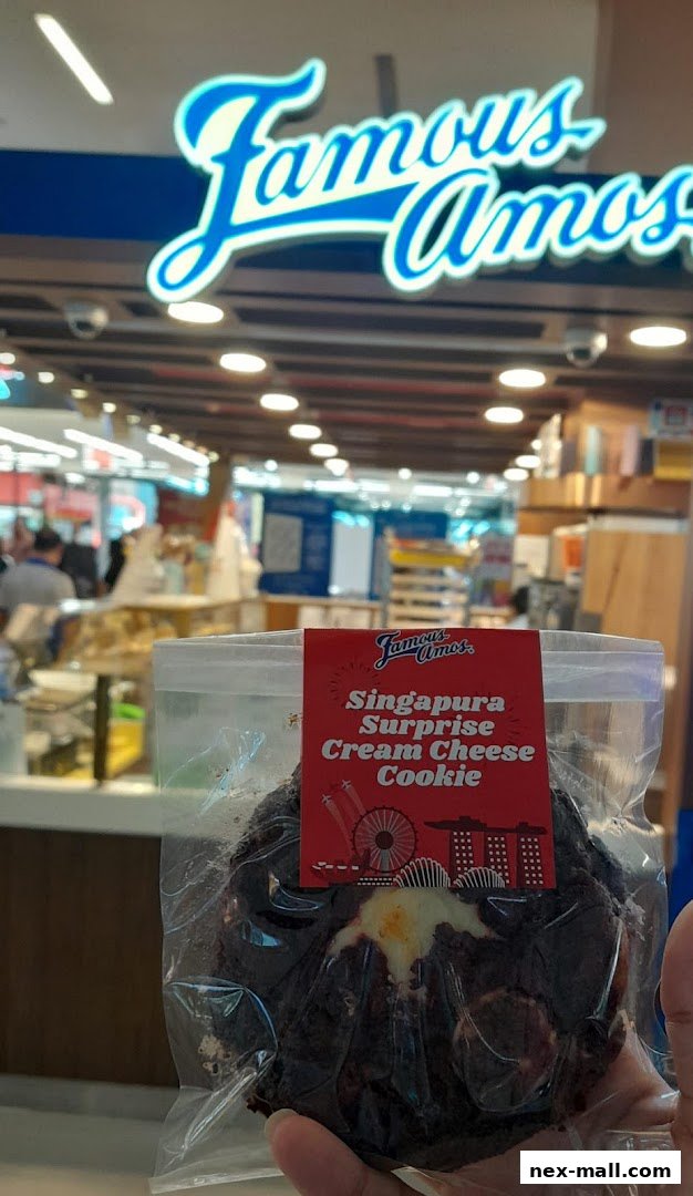 A hand holds a Famous Amos cookie with a Singapore-themed label.