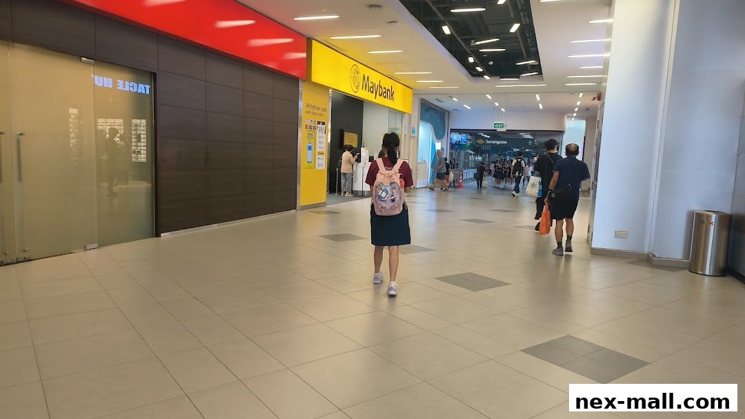 A bright yellow Maybank branch entrance with a customer walking towards it in a mall hallway.