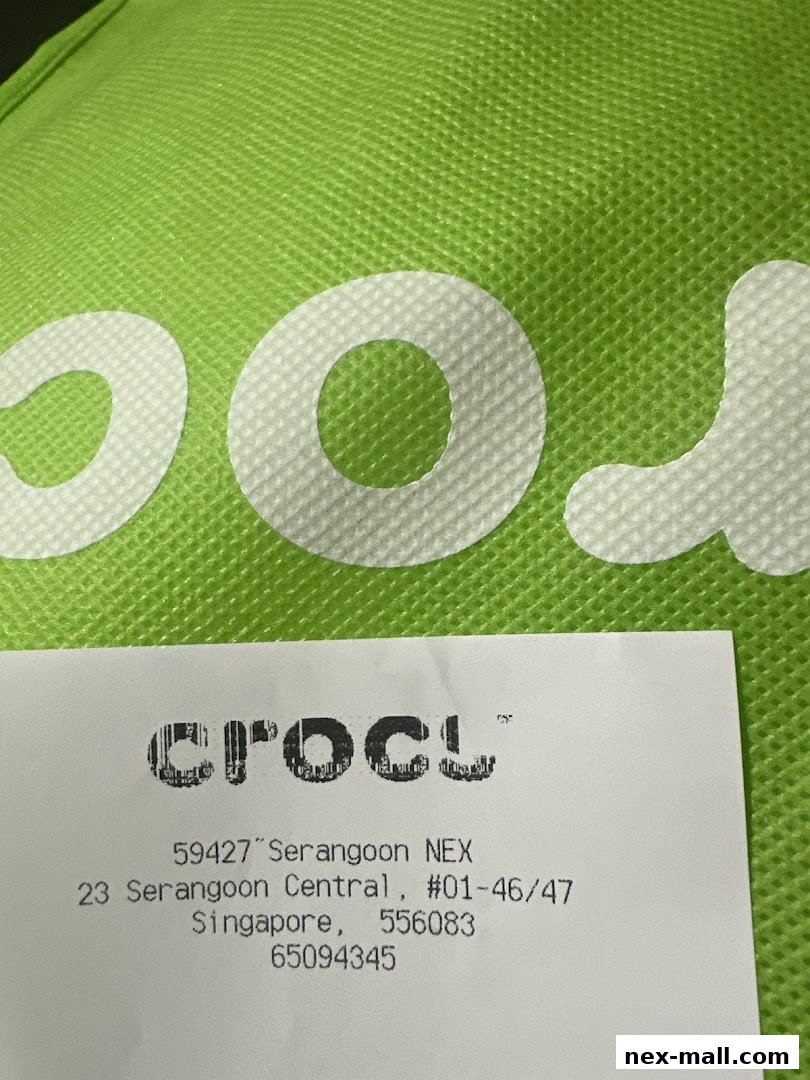 A close-up of a green Crocs bag with a receipt showing store details.
