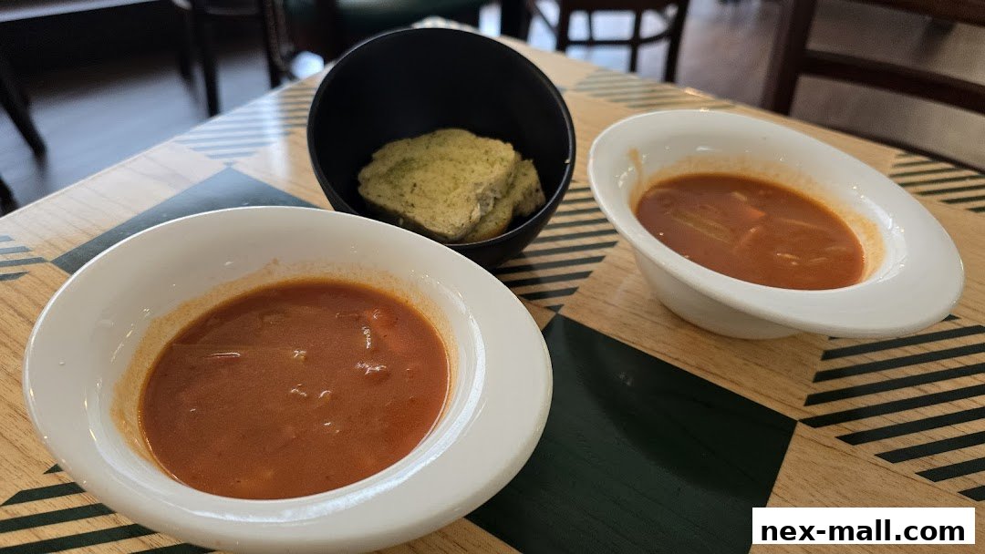 Two bowls of tomato soup and garlic bread served on a patterned table.