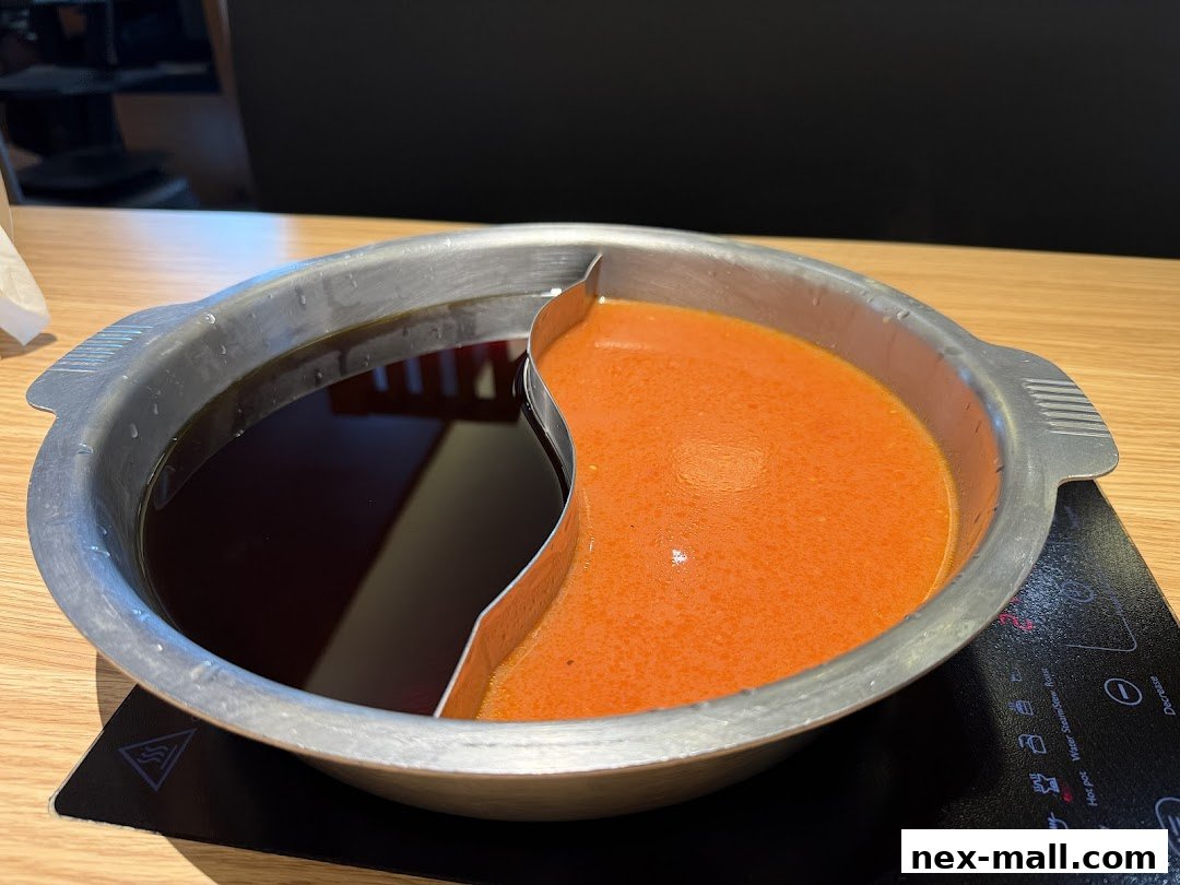 A split pot of broth, one dark and one orange, sits on a table.