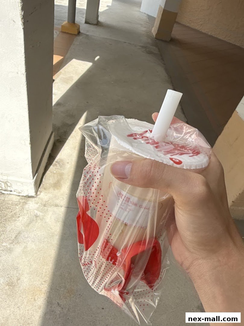 A hand holds a plastic-wrapped LiHO TEA drink with a white straw.