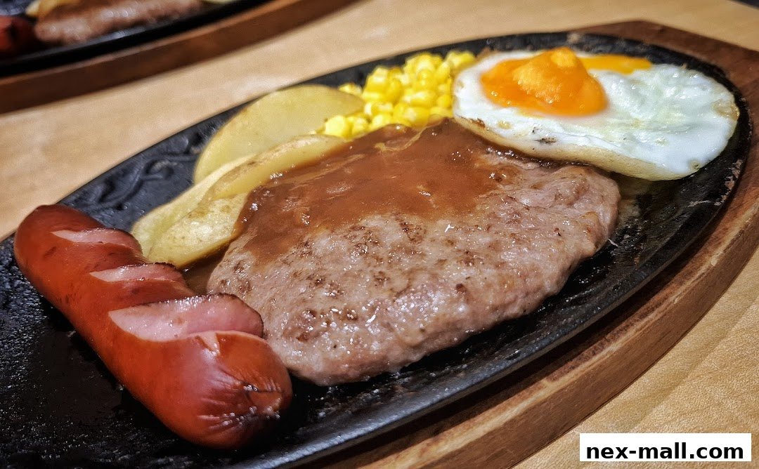 A sizzling hot plate meal featuring a hamburger steak, sausage, fried egg, corn, and potatoes.