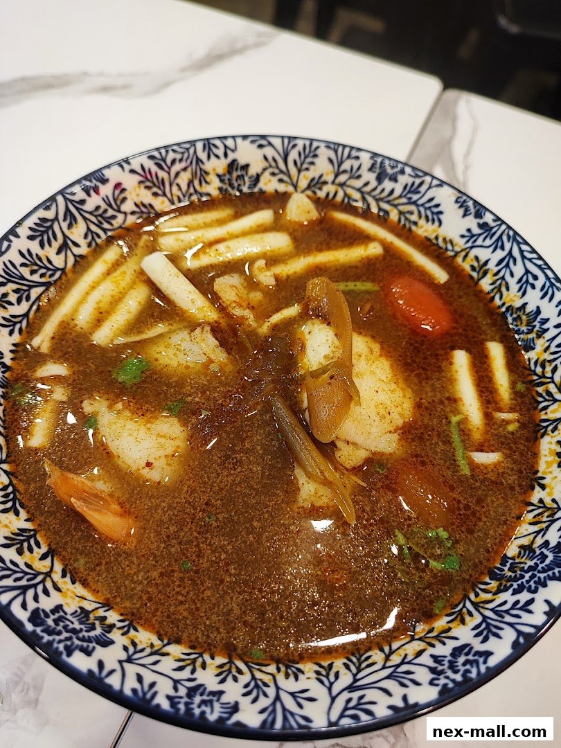 A close-up shot of a steaming bowl of Tom Yum soup with shrimp and other ingredients.