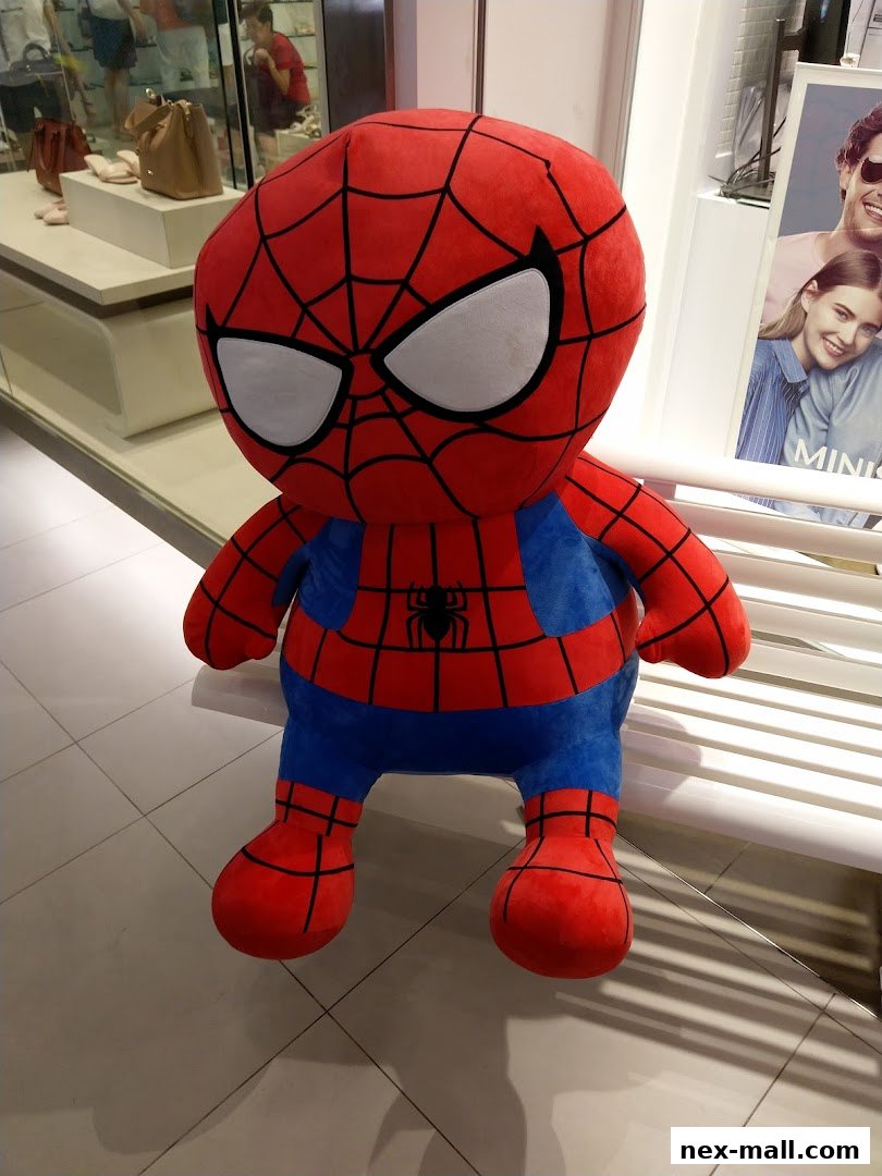 A large, plush Spiderman toy sits on a bench inside a brightly lit retail store.