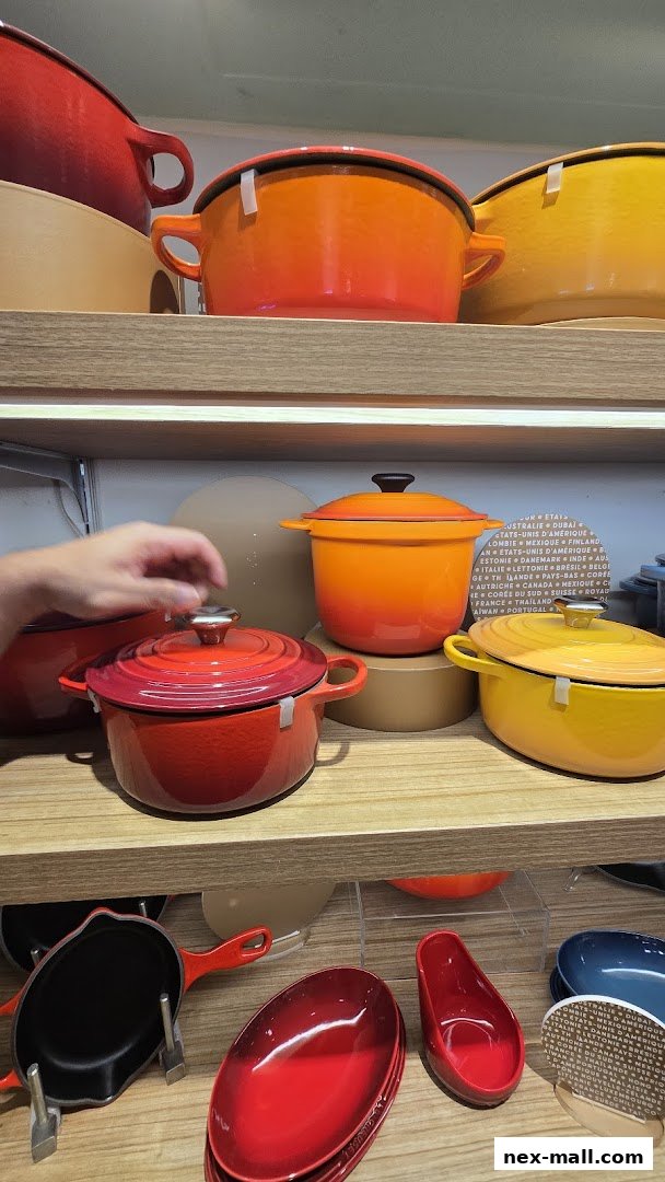 A display of colorful enameled cast iron cookware, including pots and pans, on shelves.
