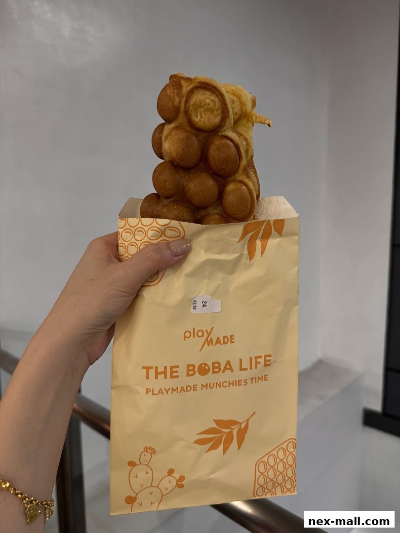 A hand holds a paper bag with a bubble waffle from PlayMade.
