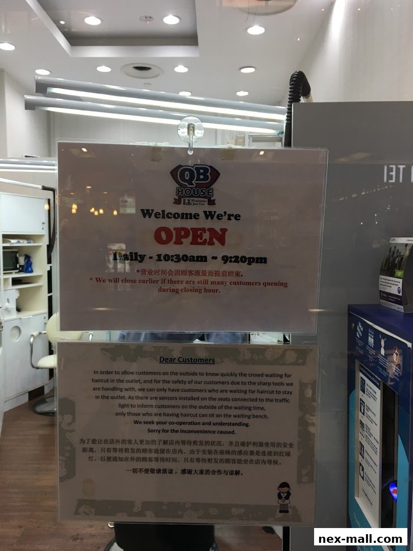 A sign on the window of QB HOUSE NEX indicating they are open with operating hours and customer information.