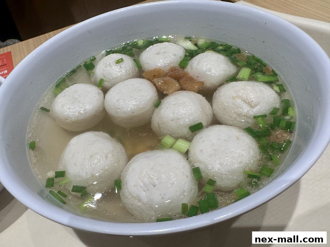A bowl of fish ball soup with chopped scallions and crispy bits.