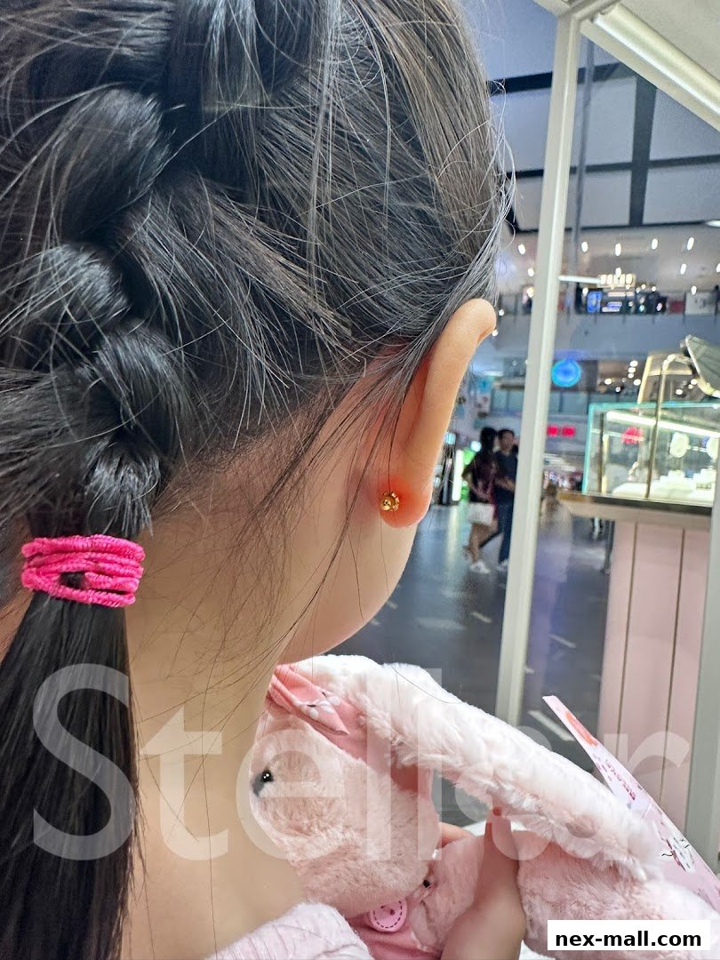 A young girl with a braided hairstyle and a gold stud earring, holding a pink plush toy.