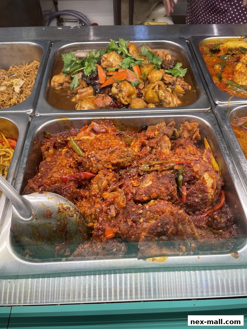 A close-up of various dishes in metal trays, featuring chicken and spicy meat.